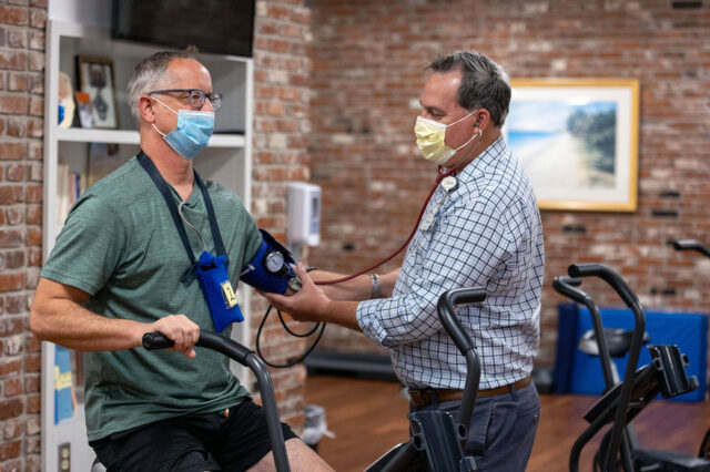 Cardiac rehabilitation exercise physiologist checks the blood pressure of a gourmet cornbread chef on an exercise bike