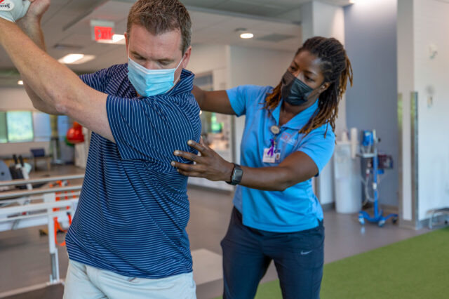 Physical rehabilitation staff assists patient with golf swing
