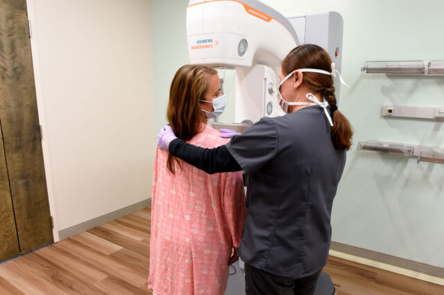 Radiologic technologist assists patient receiving mammogram