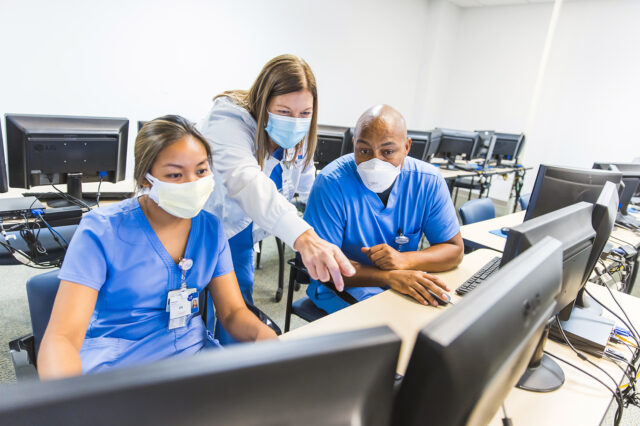 Three nurses looking at a computer screen in a training lab