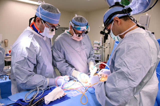 Three physicians perform spinal surgery on a patient in an operating room