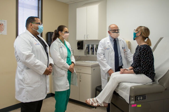 Attending and fellow gastroenterologists meet with a patient in a clinic exam room