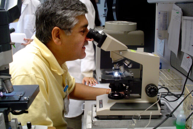 Dr. Mobeen Rathore looks into microscope in a laboratory.