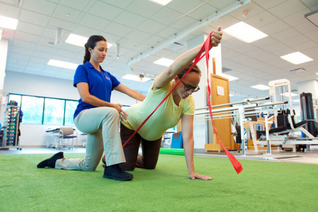 UF Health physical therapist assists patient with elastic band exercise
