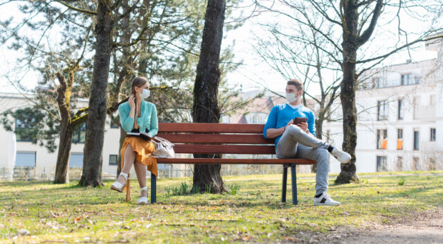 Man and woman wearing masks social distancing on bench