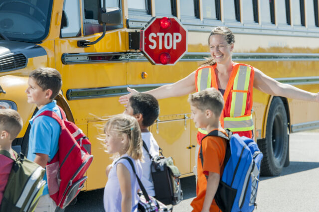 Crossing guard loading children on to stopped bus