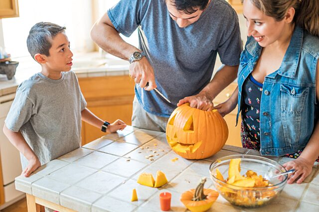 Two adults with young boy carving a pumpkin on the table
