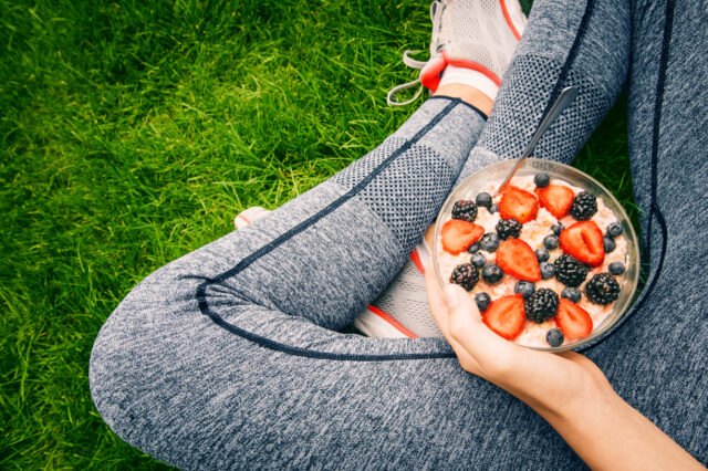 Person seated holding a bowl with oatmeal, strawberries, blueberries and blackberries