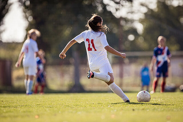 Girl running to kick soccer ball on the field