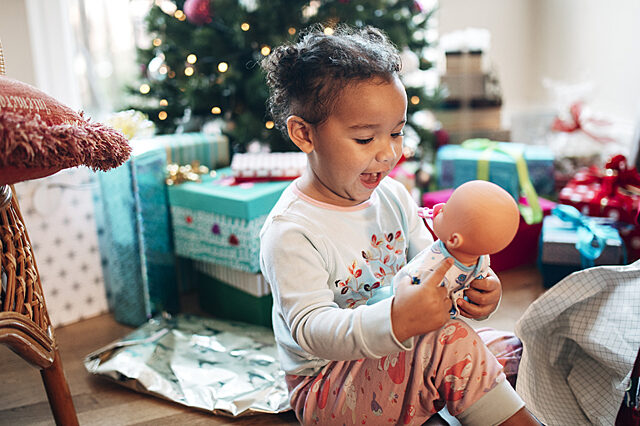 Child sitting amid presents holding a doll