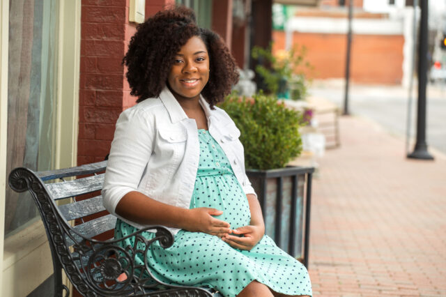 African - American Pregnant woman sitting on outdoor bench.