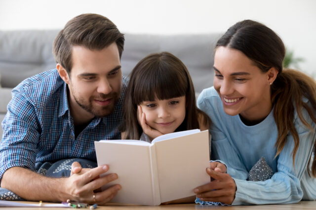 Father and mother reading a book with their young child