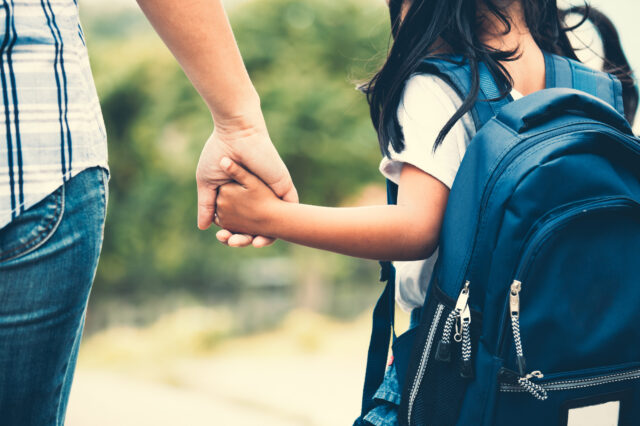 Woman holding the hand of child walking with backpack