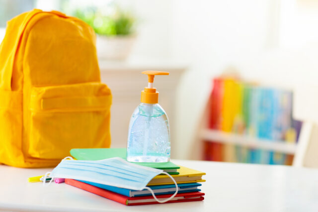Yellow backpack with books, a mask and hand sanitizer in front