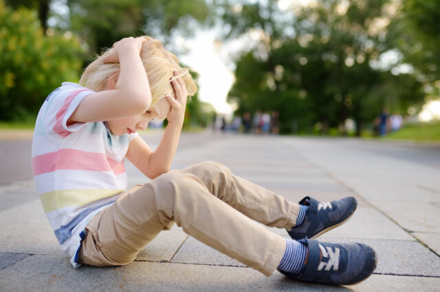 Child sitting on pavement holding his head