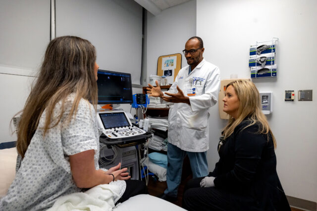 UF Health cardiovascular disease fellow and ultrasound tech meet with patient in exam room.
