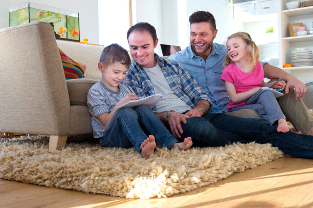 Same-sex couple with children sitting on living room floor